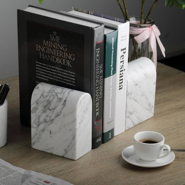 two white marble bookends in arch shape holding stack of books