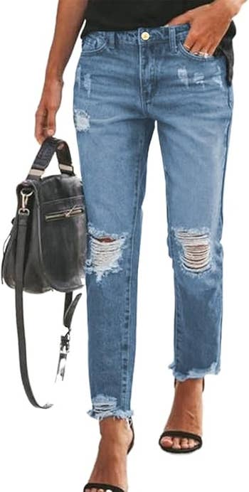 A model wearing distressed blue jeans and black sandals, carrying a black handbag