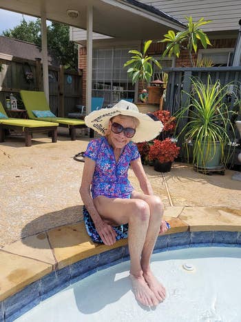 Person in a floral swimsuit and sunhat sitting by a poolside, with tropical plants in the background