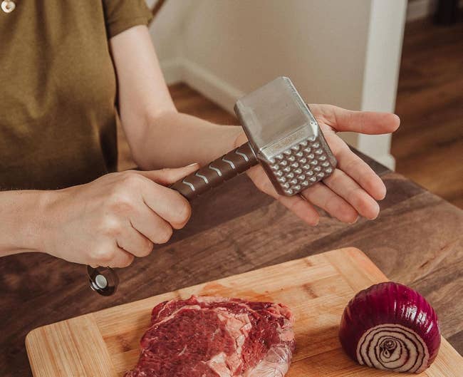 Person utilizing nutrient tenderizer shaped similar Thor's hammer successful a room with nutrient and an bulb connected a cutting board