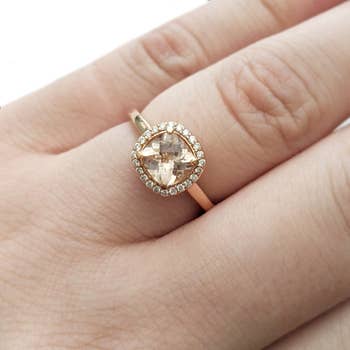 The rose gold ring on a model's finger with a cushion cut morganite and halo of diamonds around it