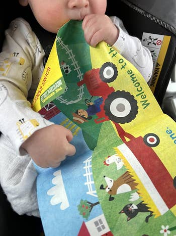 Child in a car seat holding a colorful book with farm and vehicle illustrations