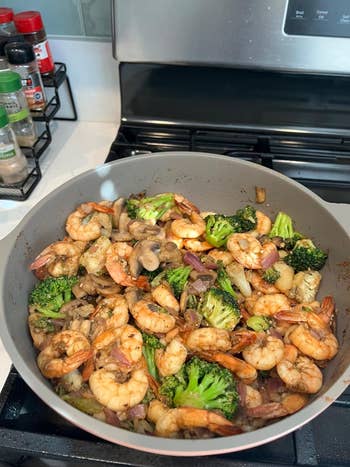 A skillet with sautéed shrimp, broccoli, and mushrooms on a stove, useful for a cooking-related shopping article