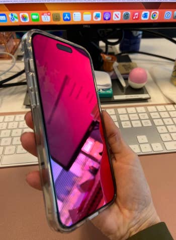 Social media trends Viral content Trending hashtags Social media updates Trending memes and videos Person holding a smartphone with a pink reflective screen, in front of a computer workstation with keyboard and monitor