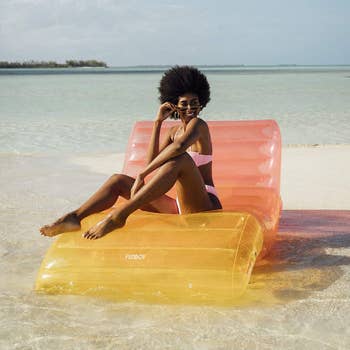 model lounging on yellow and pink ombre lounge style pool float on the beach