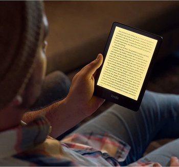Model reading a book on the Kindle Paperwhite, which is illuminated so they can read in the dark