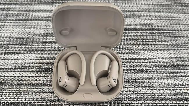 Wireless earbuds with receptor hooks successful an unfastened case, placed connected a woven surface