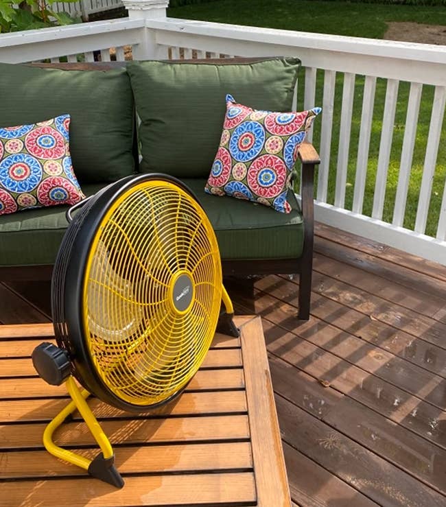 a reviewer photo of a fan sitting on a table on a backyard deck 