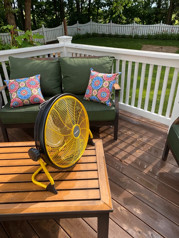 a reviewer photo of a fan sitting on a table on a backyard deck 