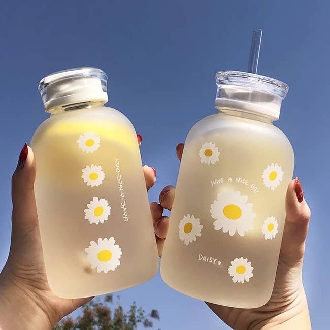 a model holding two water bottles with daisies on them. one has a screw top and the other has a straw lid