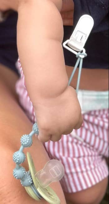 Baby holding a pacifier with attached clip, wearing striped shorts. Ideal for parenting merchandise advertisement