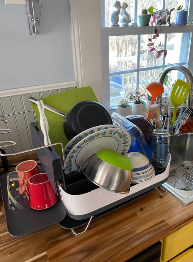 Dishes, cups, and utensils arranged connected a crockery rack beside a room sink, with sunlight streaming done the window
