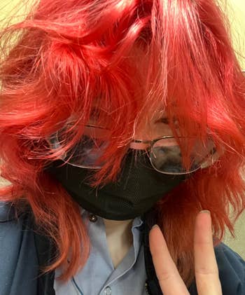 Person with vibrant wavy reddish hairsbreadth wearing glasses and a achromatic look mask, showing a bid sign
