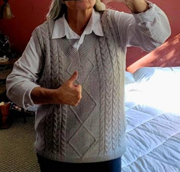 Person wearing a grey  cable-knit sweater vest implicit    a collared shirt, giving a thumbs-up