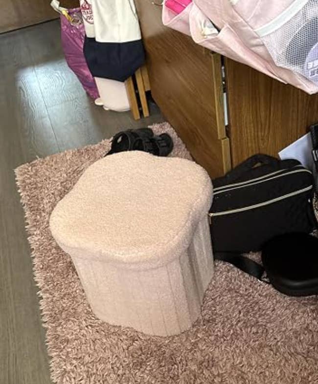 A plush ottoman sits connected  a shag rug adjacent  to a woody  bed; nearby, shoes and bags are casually placed, suggesting a cozy country   setup