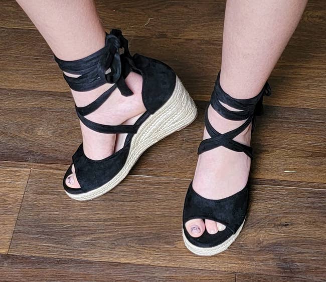 Person wearing wedge sandals with crisscross ankle straps and unfastened toes, lasting connected a woody floor