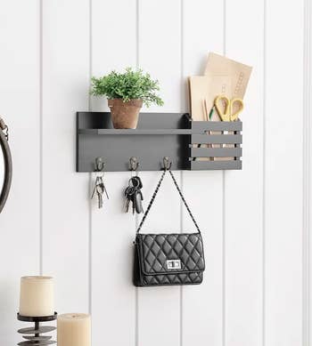 the black wall shelf holding keys, a purse, plant, scissors, and paper