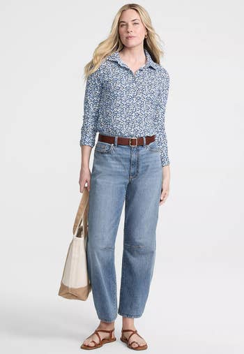 Person successful a patterned, long-sleeve garment with jeans and sandals, holding a tote bag. Casual and stylish outfit for a buying day