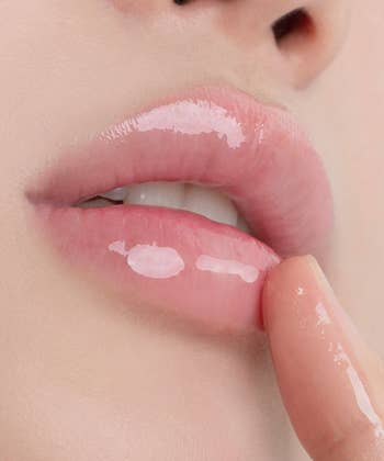 Close-up of glossy lips with a digit mildly applying a shiny articulator gloss