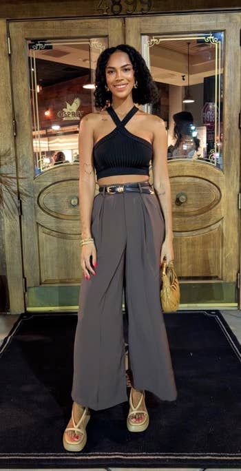 Person successful chic, casual outfit with a achromatic halter apical and wide-leg pants lasting extracurricular a rustic store entrance, holding a tan container and wearing sandals