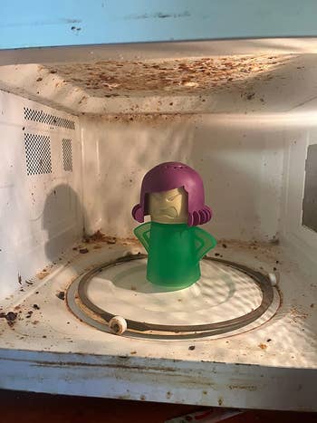 Reviewer's dirty microwave interior with green and purple angry mama steam cleaner on turntable