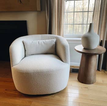 Modern surviving  country   with a round, plush armchair and a tiny  woody  broadside  array  with a decorative vase. Neutral-toned decor and earthy  airy  from the window