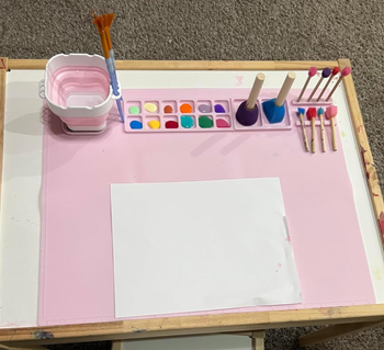 a reviewer's pink paint station with a water cup and paints and place for brushes
