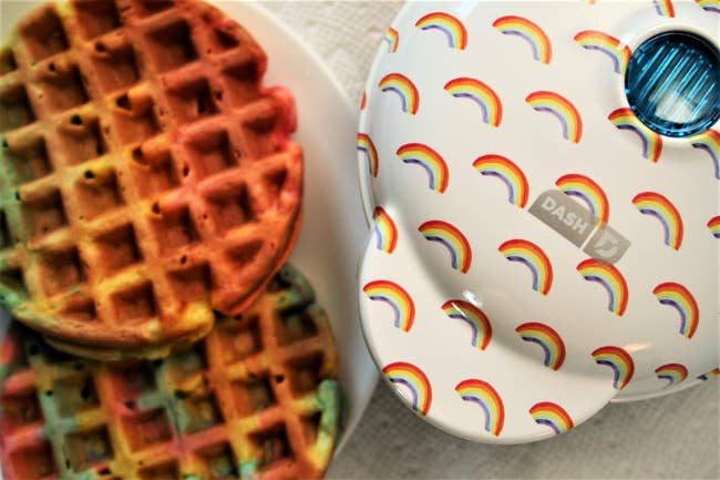 Mini waffle maker with rainbow design next to plate of multicolored waffles