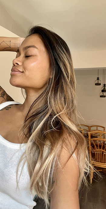 Reviewer with brown and blonde hair wearing a white tank top in front of wooden table set
