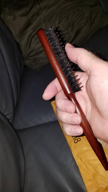 A reviewer holding a wooden-black bristle hairbrush