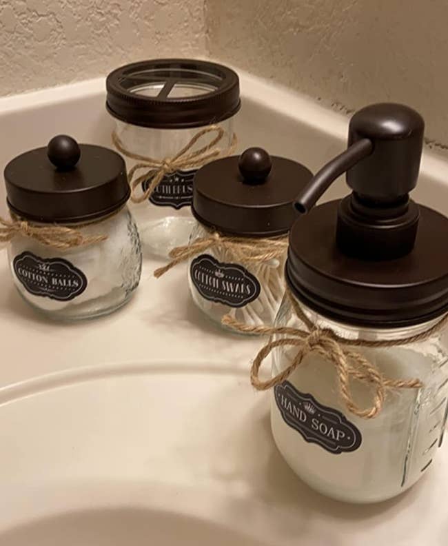 The clear glass holders with dark brown lids on a bathroom counter 