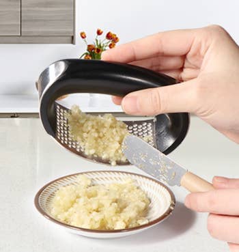 A model's hands holding the garlic press and empty the garlic pieces into a small bowl