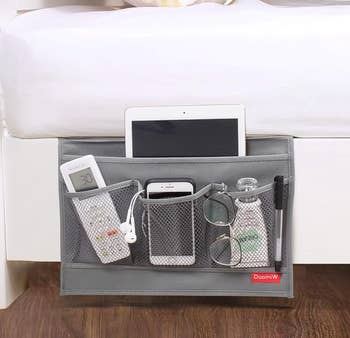 Bedside retention  caddy with pockets holding a remote, tablet, phone, glasses, and a h2o  bottle, perfect  for organized bedside retention  solutions
