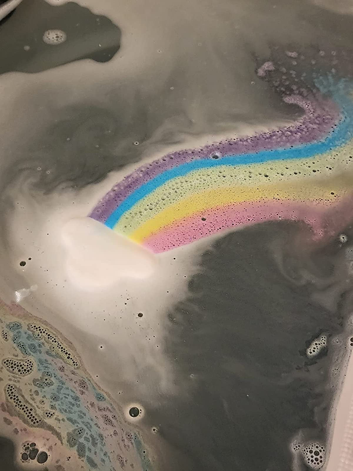 the cloud-shaped bath bomb dissolving in a tub, leaving a rainbow trail