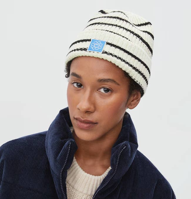 Model wearing black and white striped knit beanie with navy blue corduroy puffer jacket and white sweater