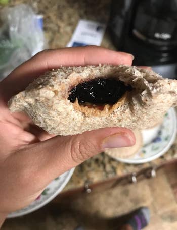 Reviewer holding up round crustless sandwich with peanut butter and jelly inside 