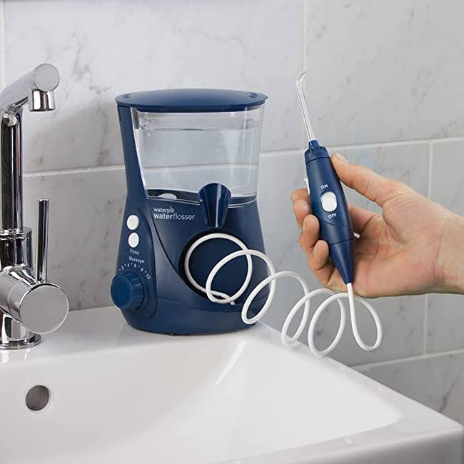 A navy blue waterpik with a well for water and a wand that fits in the palm of a model's hand 