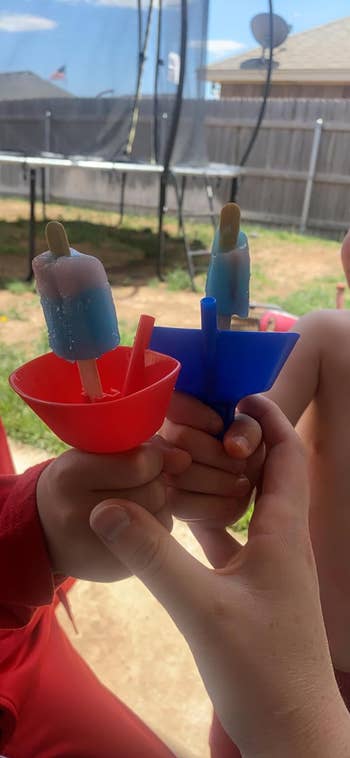 reviewer's two kids holding popsicles with the drip catches attached