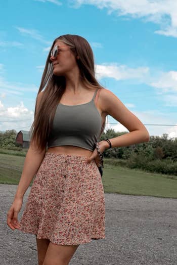 reviewer in sunglasses, a cropped tank top, and floral skirt, standing outdoors