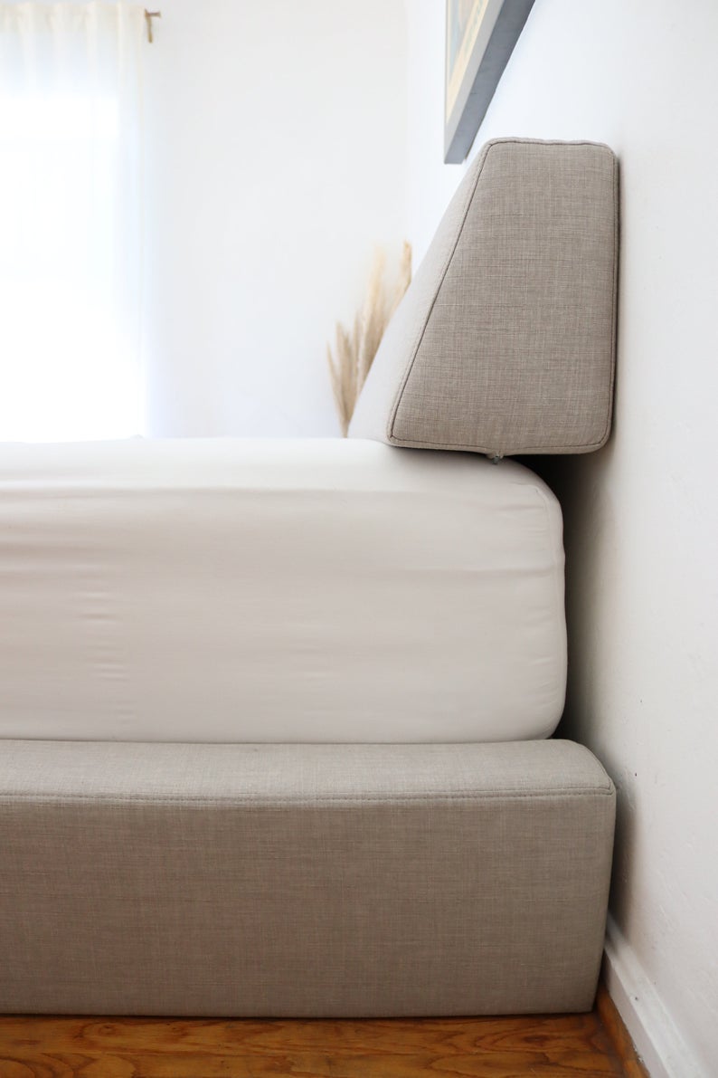 side view of a bed with a bolster pillow up against the wall