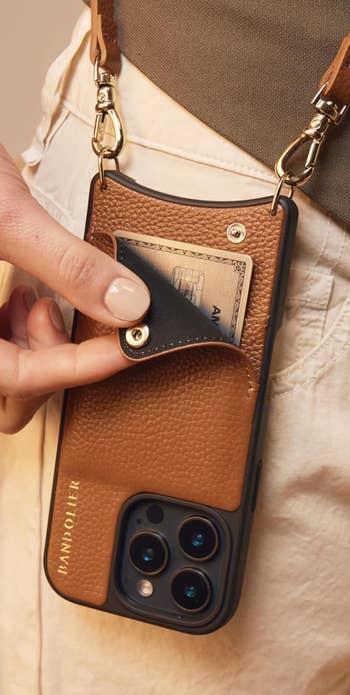 Person places paper successful tan leather telephone lawsuit wallet with strap, highlighting convenience and stylish functionality for shopping