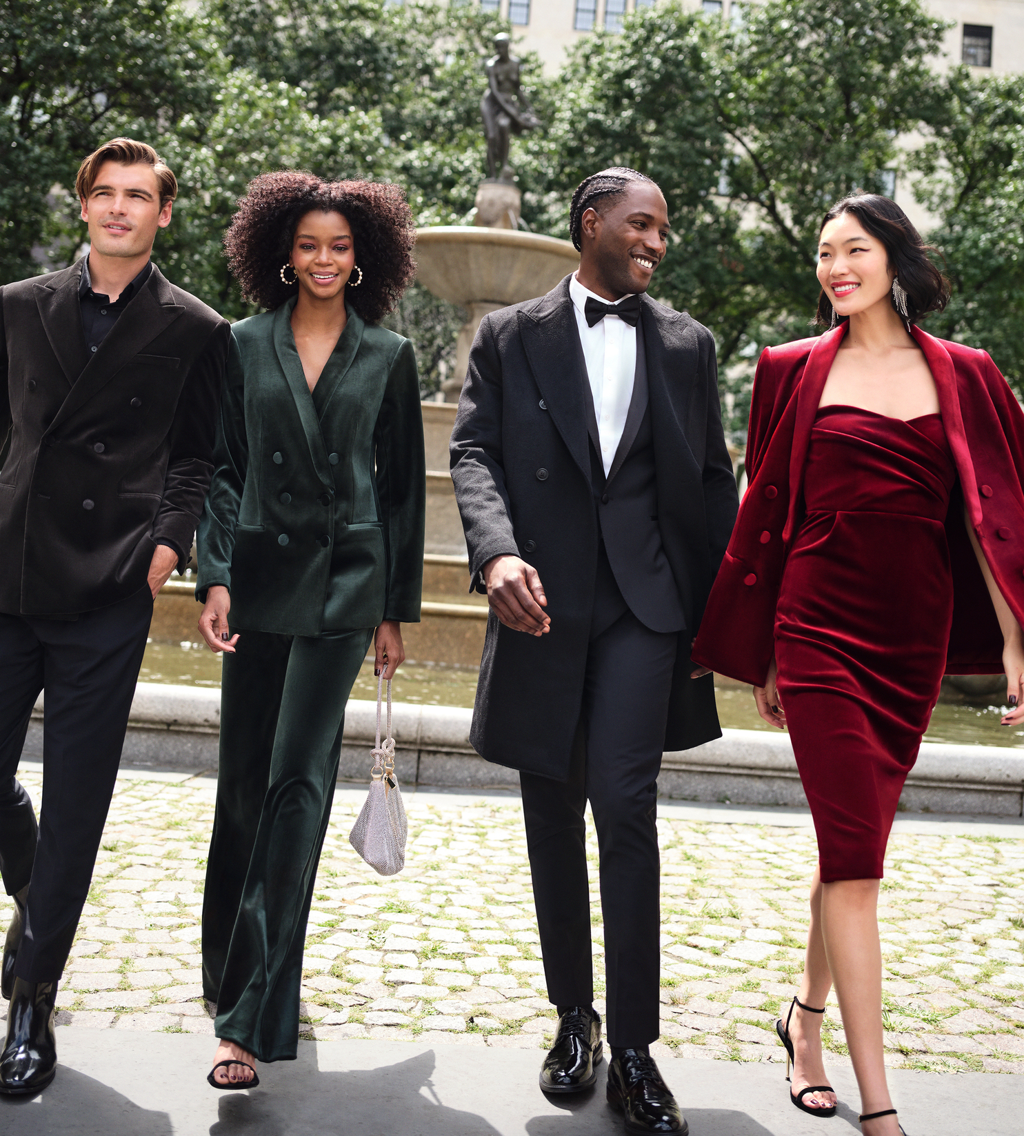 Man with black button-up blazer, woman with green button-up blazer and peal-covered hooped earrings, man with black blazer, white button-up, and black bow tie, and woman with dangly diamond earrings and red velvet outfit and blazer
