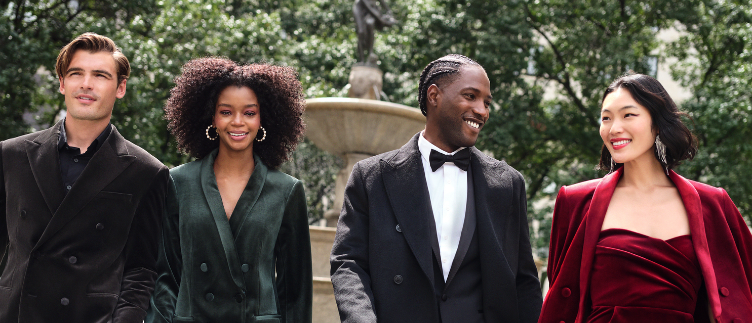 Man with black button-up blazer, woman with green button-up blazer and peal-covered hooped earrings, man with black blazer, white button-up, and black bow tie, and woman with dangly diamond earrings and red velvet outfit and blazer