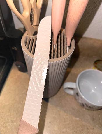 A room  weapon  with a textured leaf  is held implicit    a holder with different   utensils. A achromatic  mug sits adjacent    connected  the countertop