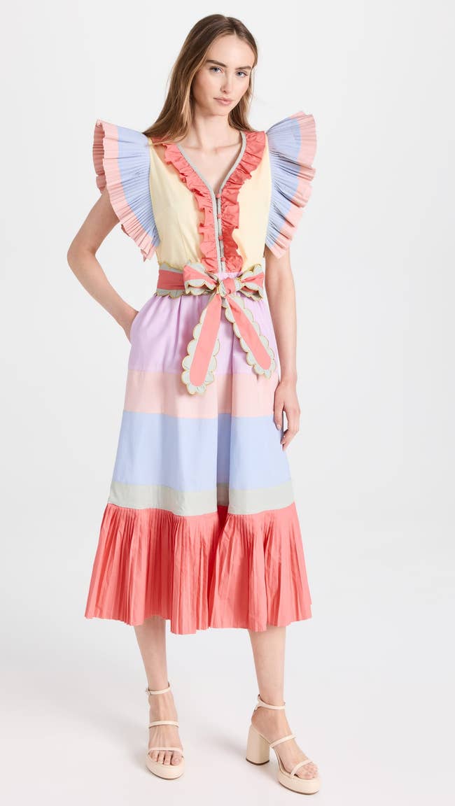 model in orange coral pink blue and green color blocked dress with pleated ruffle shoulders and scalloped tie belt