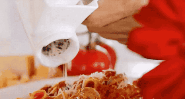 A gif of a hand turning the grater and showering parmesan on a plate of pasta