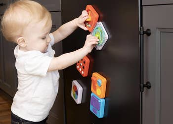 Toddler playing with colorful, interactive magnetic toys connected  a metallic  surface, engaging with antithetic  shapes and activities