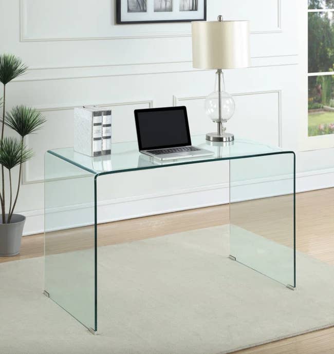 A sleek, modern glass desk with a laptop and decorative items in a bright room, ideal for a stylish home office