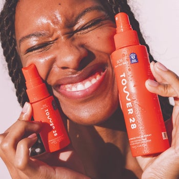 a model holding two different-sized red bottles of the facial spray up to their face