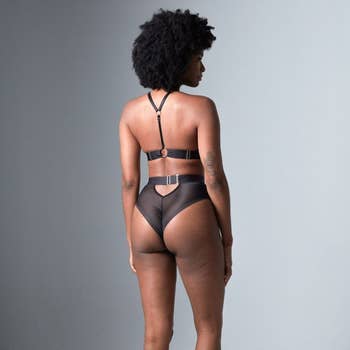 Model showcases back of high-waisted sheer lingerie with strap details